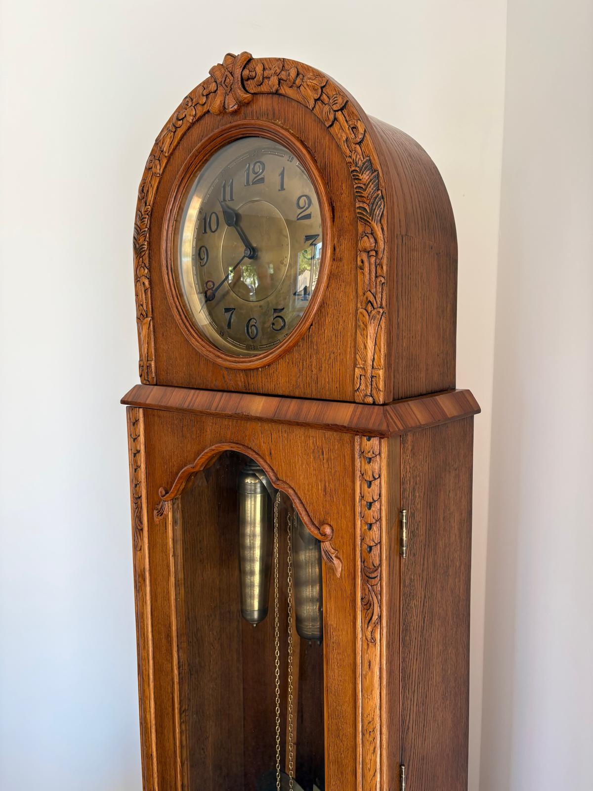 Fertige Standuhr in Frontansicht mit Ziffernblatt, geschnitztem Kopfbereich und heller gewordener Holzoberfläche.