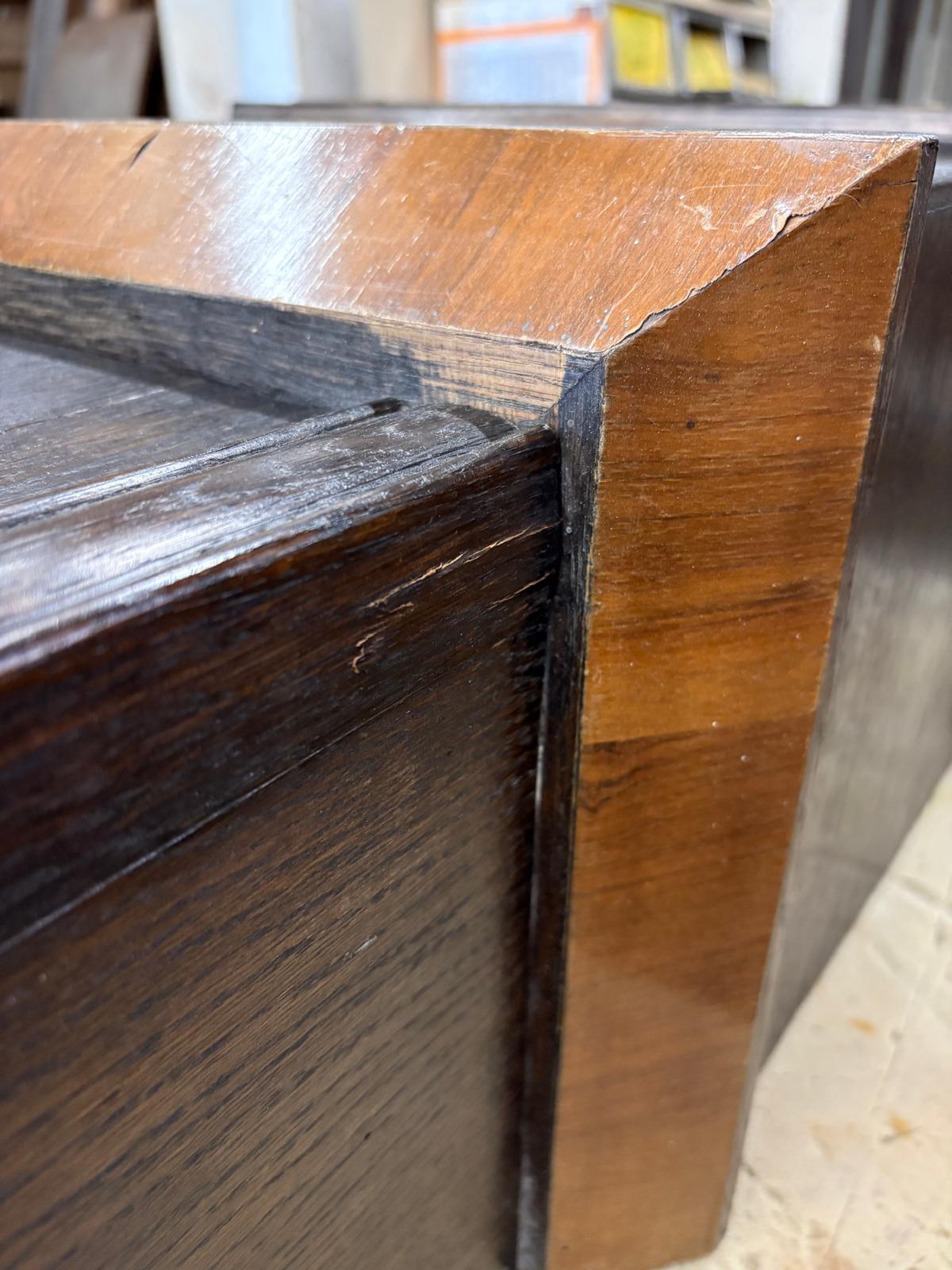 Seitliche Nahaufnahme einer Standuhr-Kante mit Furnierfehlstelle zwischen dunkler Fläche und hellerem Holz.